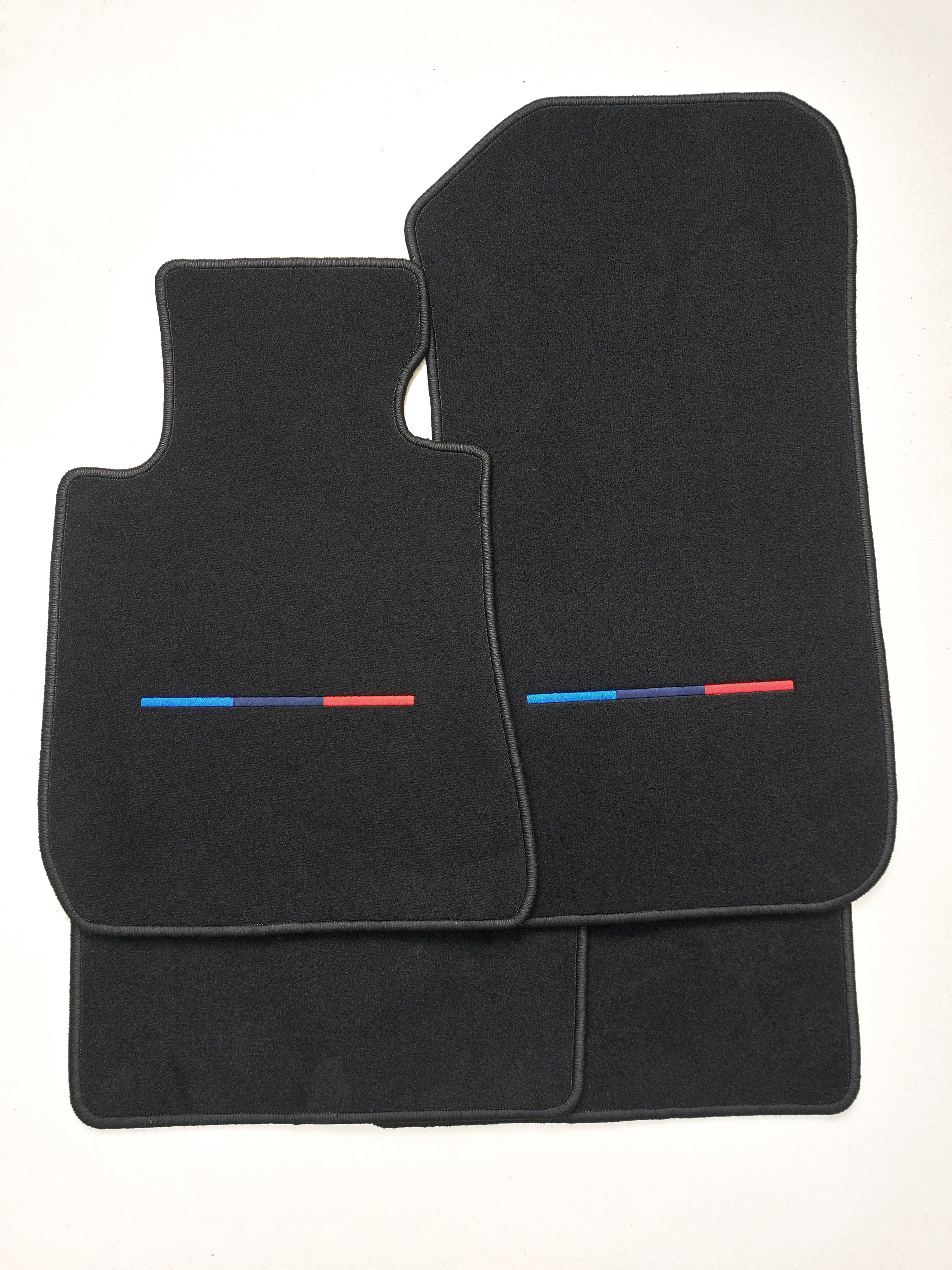 Vier bestickte Fussmatten für einen BMW in den M Farben mittig. Der Teppich ist schwarz.